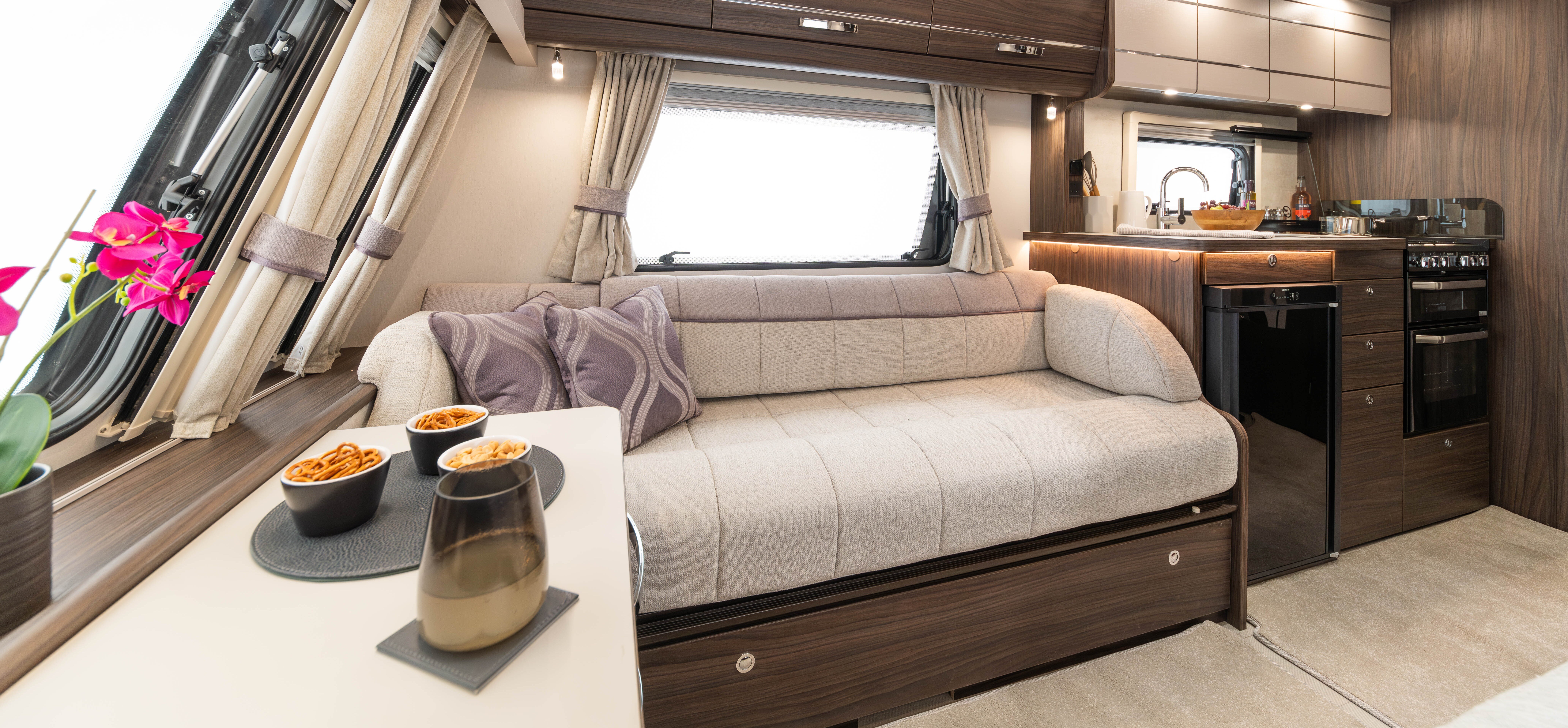 Modernly furnished caravan with a cozy seating area, kitchenette, and large windows.